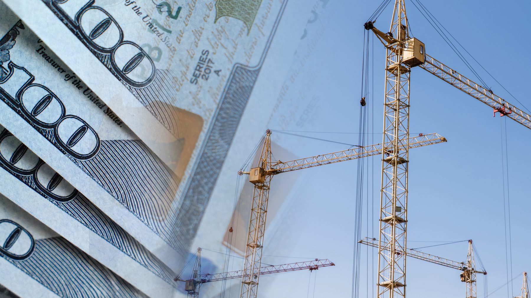 Construction cranes rising against a blue sky beside a fan of hundred-dollar bills