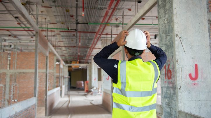 Construction superintendent in a hard hat and safety vest with his hands on his head inside an unfinished commercial building