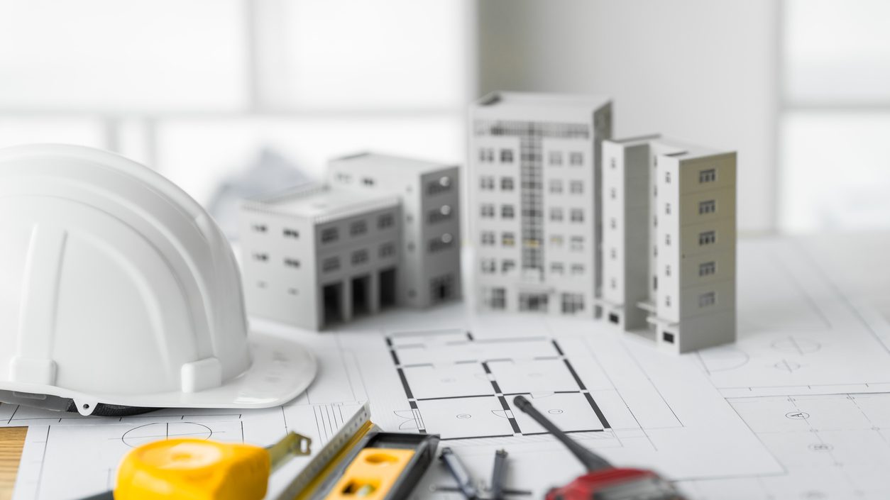 White massing models of buildings on a site plan beside a hard hat and measuring tools