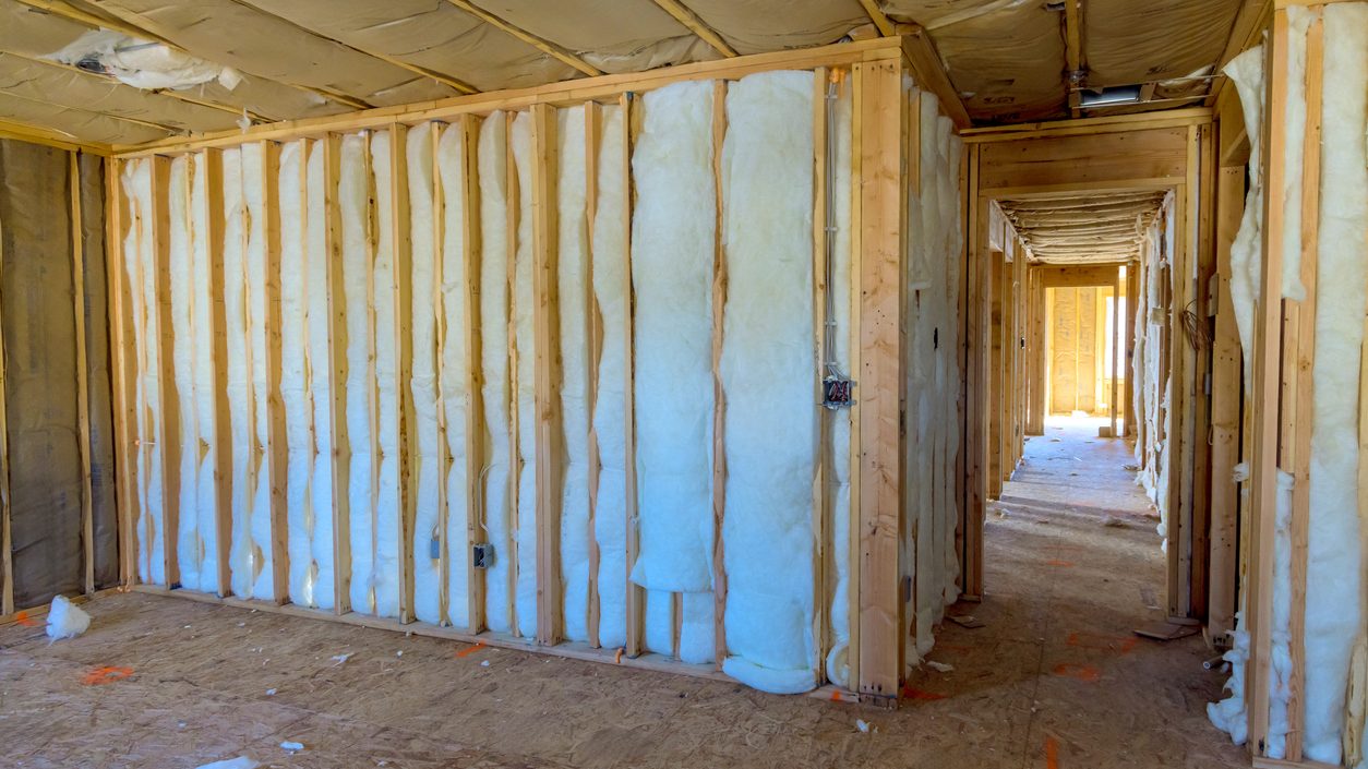 Wood-framed walls of a new home filled with insulation, looking down an unfinished hallway