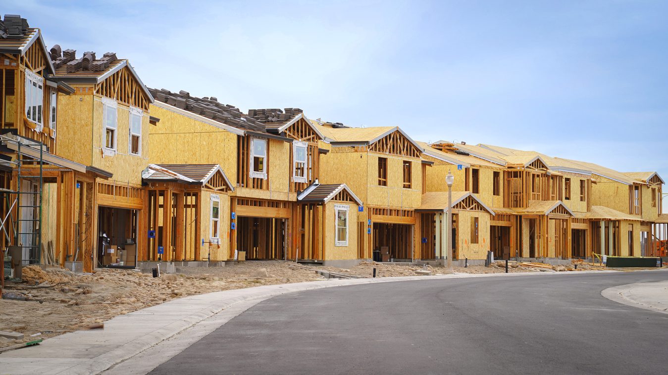 Row of new homes framed and sheathed along a freshly paved street
